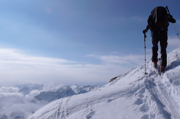 backcountry skier hikes and climbs to a remote mountain peak in Switzerland on a beautiful winter day