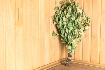 Green birch broom stands on a shelf in the corner of the bath