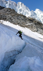 mountain climber crosses over a large and deep crevasse or bergschrund as he begins his climb of a steep north face of ice and snow in the Alps