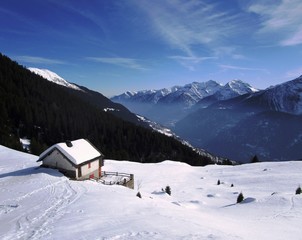 Casetta sulla neve con montagne e cielo blu