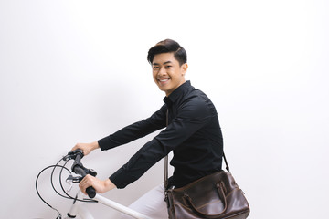Young handsome asian man against the backdrop of white wall sits on a bicycle