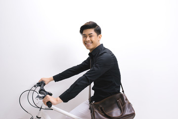 Obraz premium Young handsome asian man against the backdrop of white wall sits on a bicycle