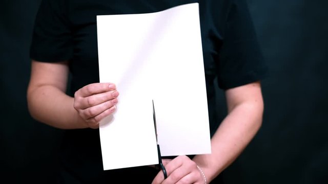 Closeup of hands with a sheet of paper on a color background. Scissor sheet of white paper lengthwise.