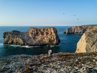 Aerial drone photograph of a couple admiring the rugged coastline at Cape St. Vincent ofthe Algarve...