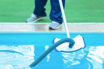 Male worker cleaning outdoor pool with underwater vacuum