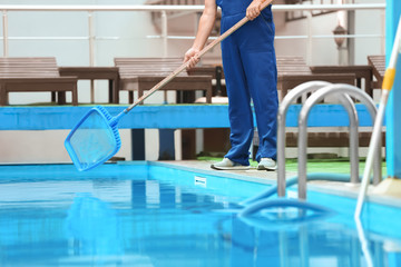 Male worker cleaning outdoor pool with scoop net