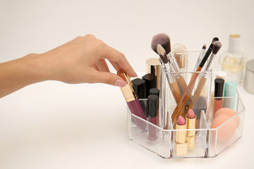 Woman taking lip gloss from organizer for makeup cosmetic products on dressing table