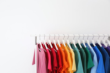 Rack with bright clothes on white background. Rainbow colors