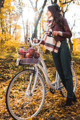 Fototapeta na wymiar low angle view of stylish woman in leather jacket and beret carrying bicycle in yellow autumnal forest