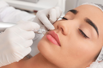 Young woman undergoing procedure of permanent lip makeup in tattoo salon, closeup - obrazy, fototapety, plakaty