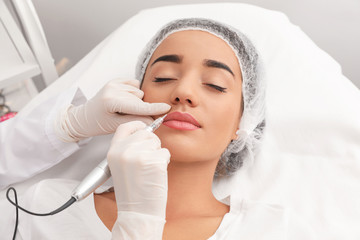 Young woman undergoing procedure of permanent lip makeup in tattoo salon