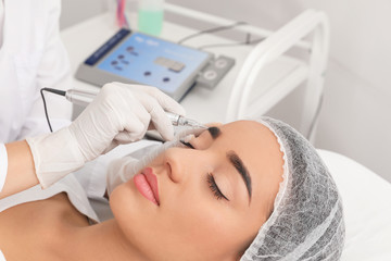 Young woman undergoing procedure of permanent eyebrow makeup in tattoo salon