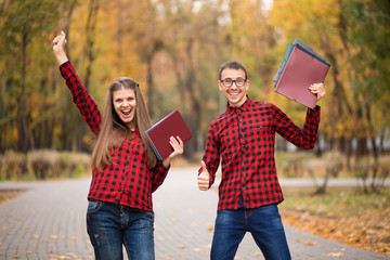 Two excited students with hands up and approved exams in autumn