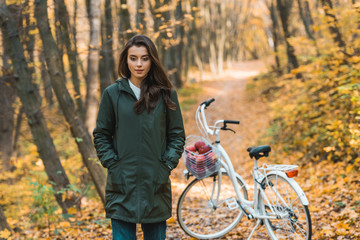 Fototapeta premium beautiful young woman walking near bicycle in autumnal forest