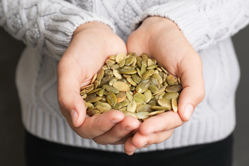 Woman holding raw pumpkin seeds, closeup view