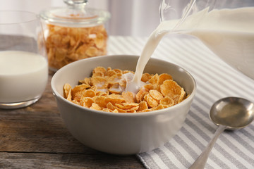 Pouring milk into bowl with healthy cornflakes on table