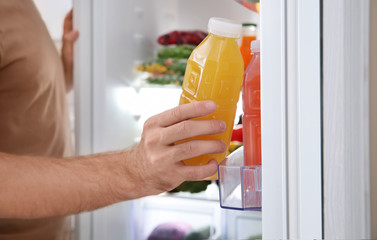 Man taking bottle with juice out of refrigerator in kitchen, closeup