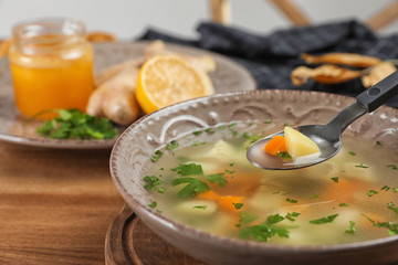 Spoon with fresh homemade soup to cure flu over bowl on wooden table