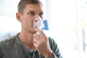 Young man using asthma machine indoors. Space for text
