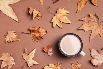 Flat lay composition with hot cozy drink and autumn leaves on color background