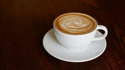 Hot coffee latte cappuccino spiral foam in ceramic cup on dark wooden table background