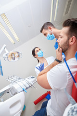 Portrait of a handsome young patient in pain with the dentist and his assistant.