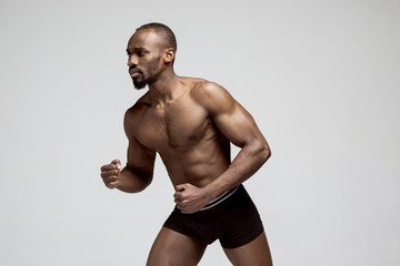 Fototapeta na wymiar Fit young man with beautiful torso, isolated on gray background. The naked torso of African American man posing at studio. The muscular body, fitness, sports, healthy lifestyle and bodybuilder concept