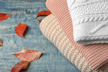 Fototapeta na wymiar Stack of folded knitted sweaters and autumn leaves on table. Space for text