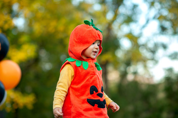 The boy dressed in an orange pumpkin costume at the Halloween party outside with black and orange balloons close up portrait 