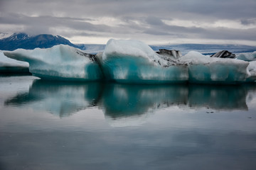 Obraz premium Beautiful big blue iceberg floating in Jokulsarlon glacial, Iceland in summer at dusk, reflecting in the water.