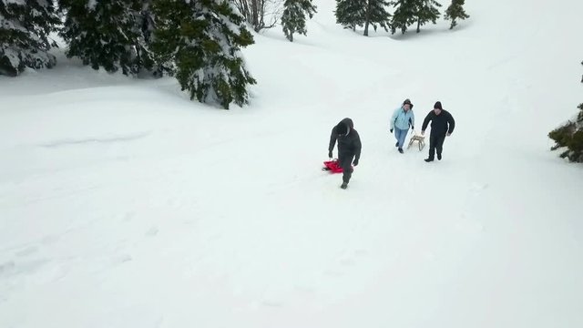 Three people are pulling sleighs uphill. It's winter time and people like to spend free time outdoors on the snow.