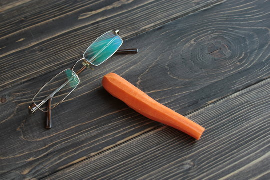 Оранжевая морковь и очки, на деревянном фоне. 