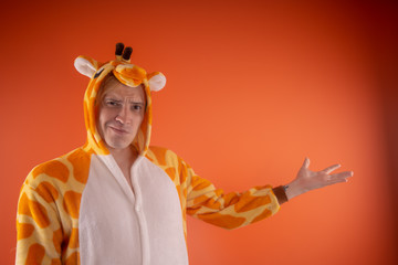 pajamas in the form of a giraffe. emotional portrait of a guy on an orange background. crazy and...