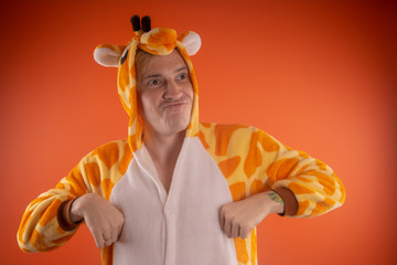 pajamas in the form of a giraffe. emotional portrait of a guy on an orange background. crazy and...
