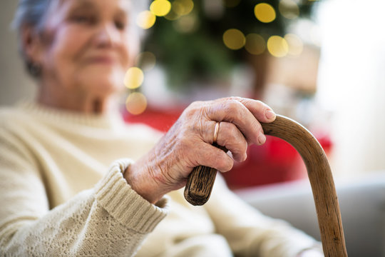 A close-up of a senior woman holding a walking stick at home at Christmas time.