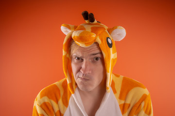 pajamas in the form of a giraffe. emotional portrait of a guy on an orange background. crazy and...