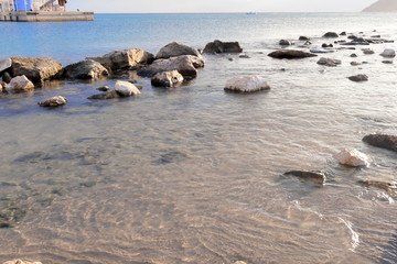 Sea shore with stones and rocks in reflected water at sunset on the horizon and harbor