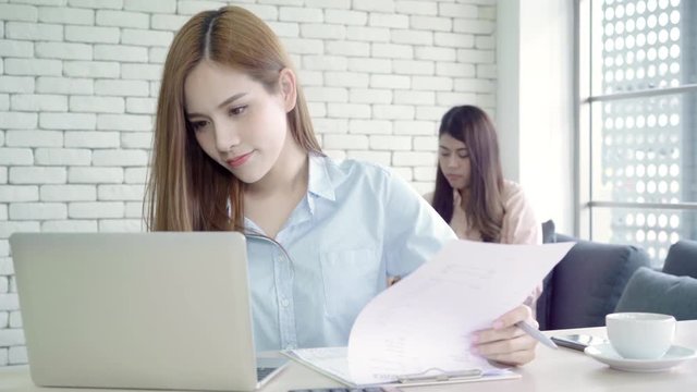 Attractive smart creative Asian business women in smart casual wear working on laptop while sitting on desk on office desk. Women work at office concept.