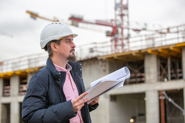 Portrait of architect at work with helmet in a construction site, reads the plan, paper projects