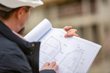 Portrait of architect at work with helmet in a construction site, reads the plan, paper projects