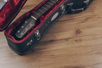 an acoustic guitar in the brown leather guitar hard case on the wooden floor