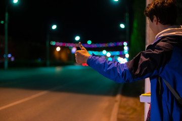 male tourist hitch-hiking the car at night in the unknown city