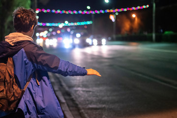 male tourist hitch-hiking the car at night in the unknown city