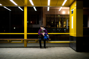 young man sit on the bus stop bench waiting in the night f