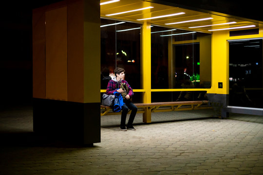young man sit on the bus stop bench waiting in the night f