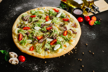 A vegeterian pizza withvagetables and herbs on black background