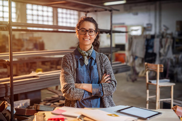 Strong confident middle aged woman engineer standing and looking at the camera at her workshop. - obrazy, fototapety, plakaty