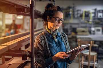 Middle aged beautiful woman standing in her work shop at looking at the tablet.