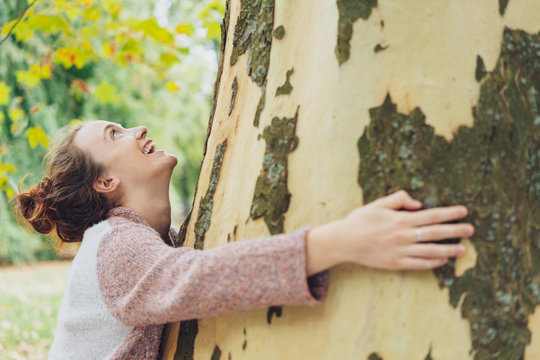 Laughing happy young woman hugging a tree