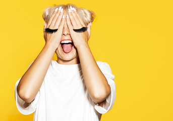 Attractive girl with eyelash on hands. Blonde cool model at studio on yellow background. Funny...
